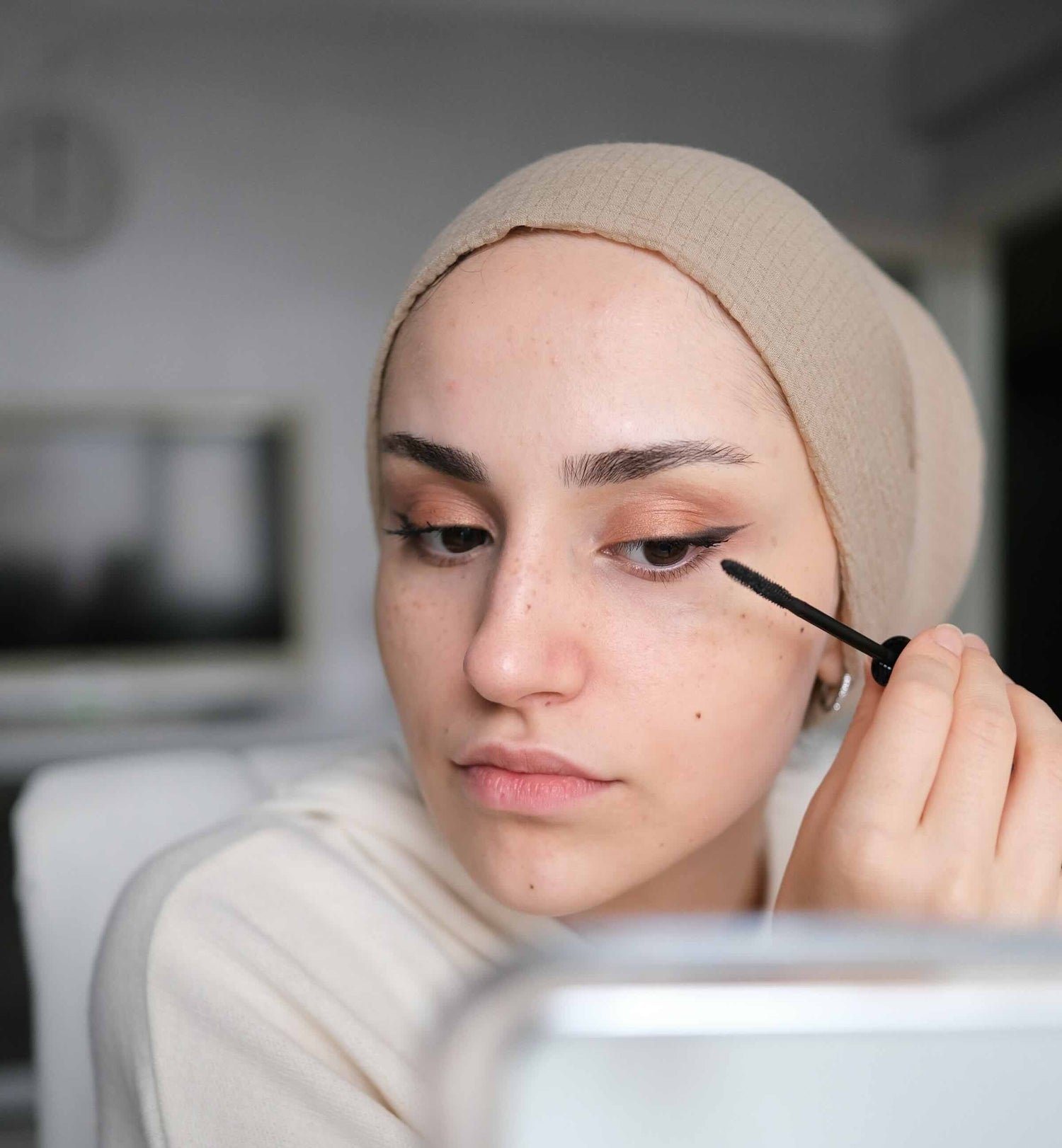 Vrouw met hoofddoek en gevoelige ogen brengt tubing mascara aan